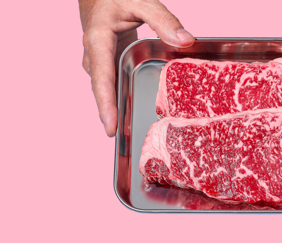 Raw meat in a metal tray held by hands against a pink background